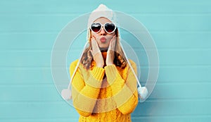 Winter portrait young woman blowing red lips sending sweet air kiss wearing yellow knitted sweater and white hat with pom pom