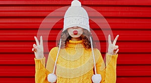 Winter portrait young woman blowing red lips sending sweet air kiss wearing yellow knitted sweater and white hat with pom pom
