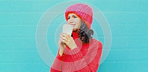 Winter portrait young woman drinking hot coffee looking away wearing a knitted sweater, pink hat on white background