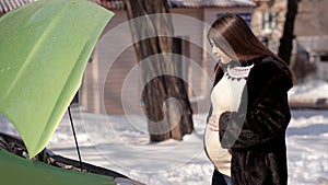 In winter, a pregnant girl is looking for help from passing cars in the repair of a failed car