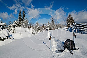 Winter remote alpine village outskirts, snow drifts on mountain fir forest edge. Tourist backpack on a freshly trodden hiking