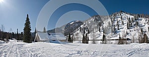 Winter resort in the mountains with blue sky. Wooden house in the snow against the background of a high mountain. Green spruce