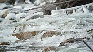 Winter river flowing near snow and ice covered stones, slow motion video detail