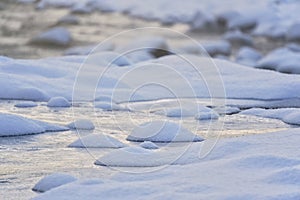 Winter river with shallow water, rocks covered with snow, closeup detail