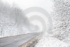 Winter road with car in fog in a snowstorm, ice and bad visibility