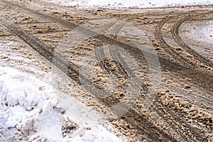 Winter road with car tracks in dirty snow and de-icing chemicals