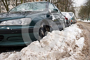 Winter. The road is covered with snow. Cars parked along the roadside and covered with snow