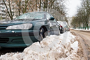 Winter. The road is covered with snow. Cars parked along the roadside and covered with snow