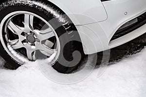 Winter on the road - the front of a white car with a tyre parked in the snow