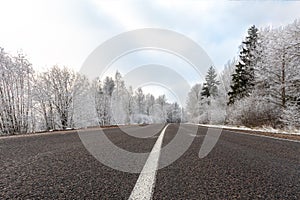 Winter road at frosty day with blue sky, landscape with snow covered trees, pattern of white highway dividing strip and ice on