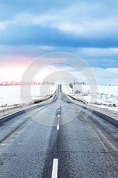 Winter road going over the horizon. Blue clouds above the road