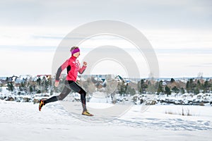 Winter running exercise. Runner jogging in snow. Young woman fitness model running in a city park