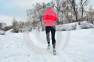 Winter running in park: back view of woman runner jogging in snow, outdoor sport and fitness