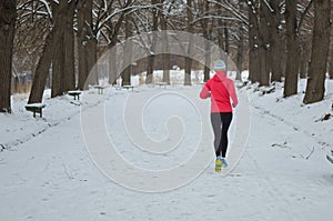 Winter running in park: happy active woman runner jogging in snow, outdoor sport and fitness