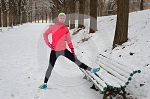 Winter running in park: happy woman runner warming up and exercising before jogging in snow, outdoor sport and fitness