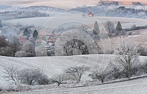 Winter Rural Landscape With With Frosted Wavy Plowed Fields, Trees In Hoarfrost And Old Windmill On The Hill. Beautiful Morning On