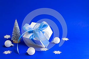 Winter sale. White gift box with blue ribbon, winter tree, Snowflakes and Silver balls in Christmas composition on blue background