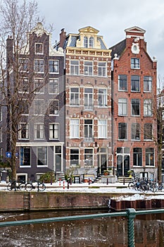 A winter scene of Amsterdam canal houses in the snow with ice on the water, vertical