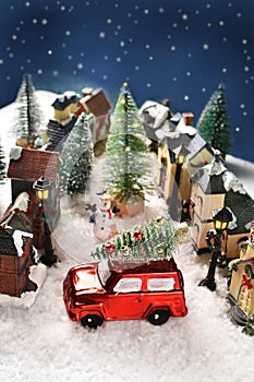 Winter scene decoration with houses in small town on Christmas night with a red car with a Christmas tree on the