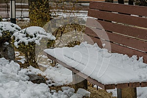 Winter scene of wooden park bench covered with snow next to snow