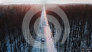 Winter scenery. Car dashing through the snow covered road surrounded by tall leafless trees