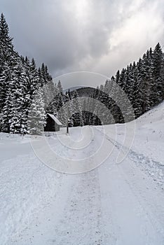 Winter scenery with snow covered road, forest, hill on the background and small wooden shelter