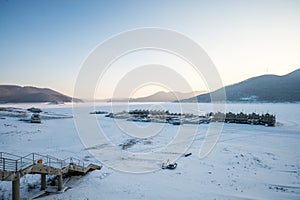 Winter Scenery of Sunset on the Lake Songhua against snow mountains and frozen lake with fog on the lake surface, Jilin Province,