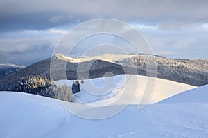 Winter scenery. Wooden fence. Beautiful landscape of high mountains, forest and sky with clouds. Lawn covered with white snow.