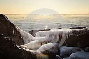Winter seascape. Stones covered with icicles on the shore and the sun
