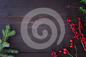 Winter season and Christmas background. Branches of fir, yew, rose hip and red barberry on rustic dark brown wooden table.