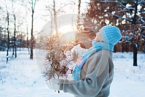 Winter seasonal activities. Senior woman throwing snow in the air at sunset in forest holding fir tree branches