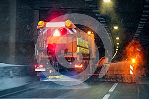 Winter service vehicle in work drives into a tunnel. Image blurred due to snow and salt