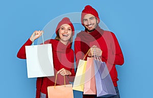 Winter Shopping. Happy Young Couple In Knitted Hats Holding Bright Shopper Bags