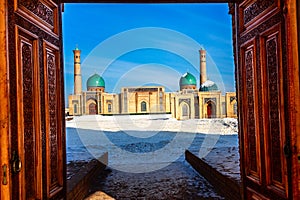 Winter shot of blue domes, mosques and minarets of Hazrati Imam medrese with wooden ornated doors in the foreground, religious