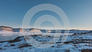 Winter in Siberia. There is snow and dry grass on the shore of a frozen lake.