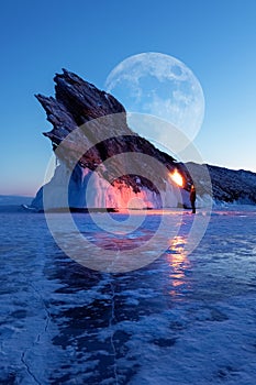 Winter Siberian landscape. Lake baikal, silhouette of a man with a torch on the background of the rock and the moon. Lake Baikal.