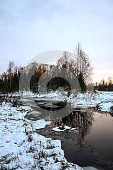 Winter Siberian landscape. The river does not freeze in winter. The reflection in the water. Sunset.