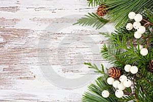 Winter side border with evergreen branches, white berries and pine cones on a rustic white wood background photo