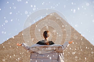 Winter snow on background of Pyramids of Cheops Egypt tourist girl in warm jacket. Concept anomalous cold cyclone