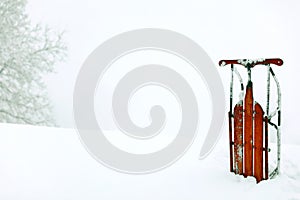A winter snow scene background with a red vintage upright sled.