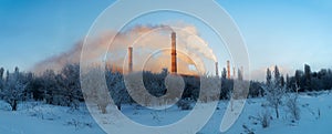 Winter snowy field with chimneys coming out of white smoke. Industrial landscape