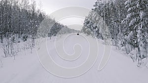 Winter snowy road leading through the coniferous forest. Clip. Man riding a snowmobile and going into a skid, extreme