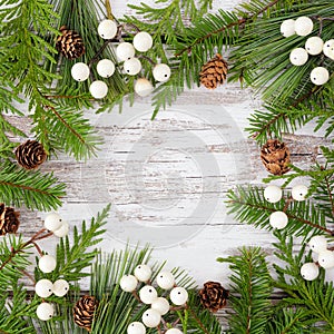 Winter square frame with evergreen branches, white berries and pine cones on a rustic white wood background photo
