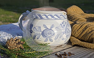 Winter still life hot smoking tea in rustic white blue painted ceramic cup with beige woollen scarf, spruce tree branches, pine co