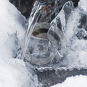 Winter stream flows through of ice and frost. Jet froze, formed icicles