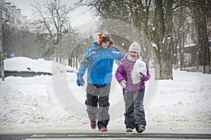 In winter, on the street in snowy weather, a boy and a girl cross the road along a pedestrian crossing