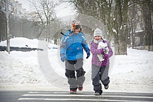 In winter, on the street in snowy weather, a boy and a girl cross the road along a pedestrian crossing