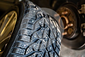 Winter studded tires in the service near the car, seasonal tire change, close-up