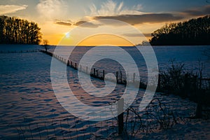 Winter sunset over a fence and snow covered farm field in rural