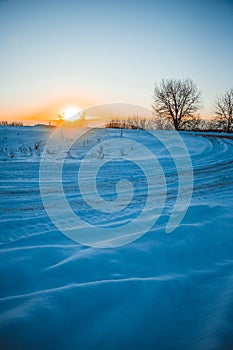 Winter sunset over the field with trees in the foreground.